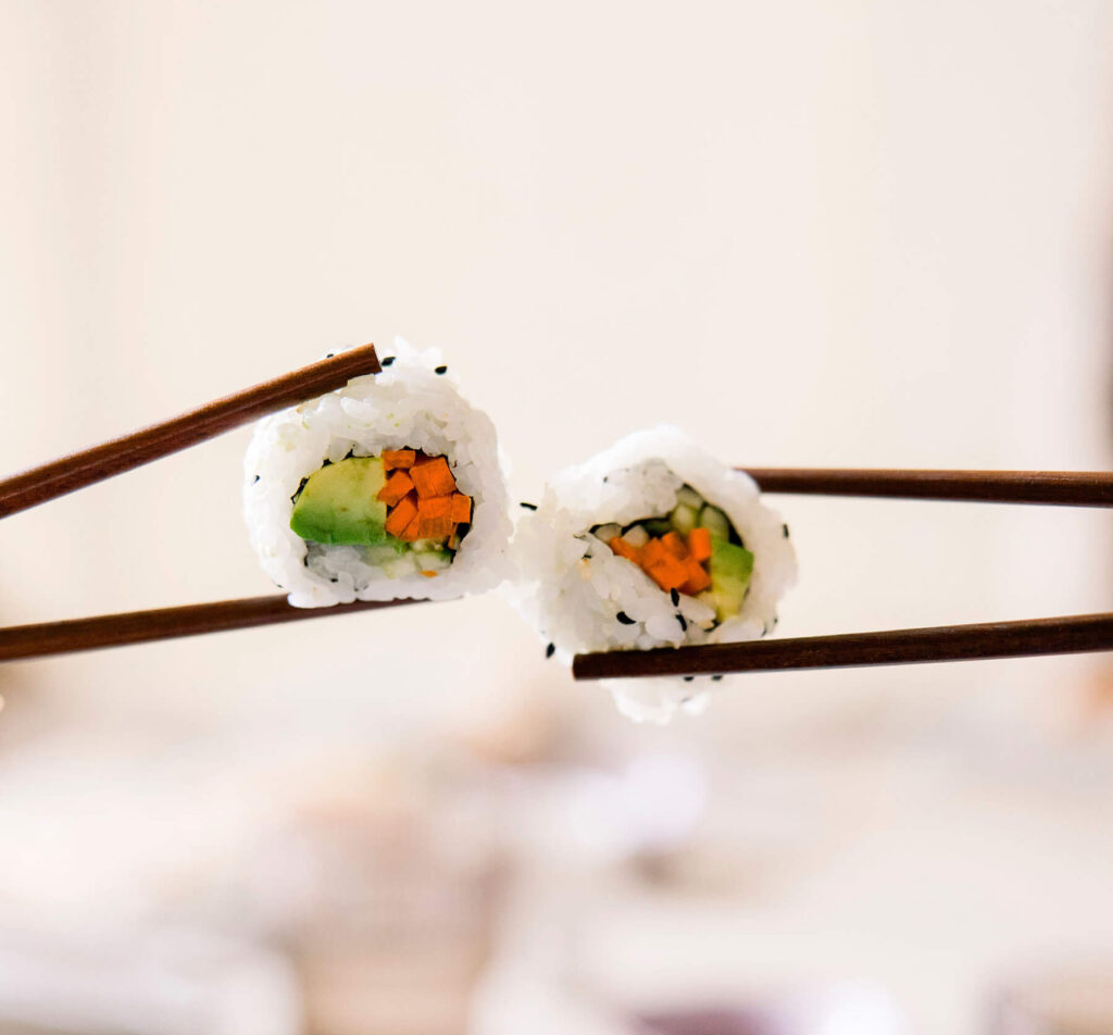 Two pieces of sushi touching, held up by chopsticks